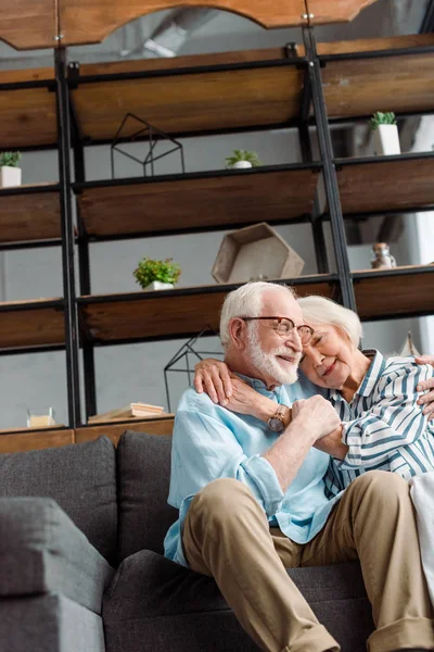 Low angle view of smiling senior couple hugging on couch at home — Stock Photo