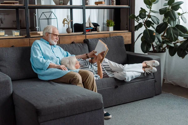 Senior couple reading book on couch in living room — Stock Photo