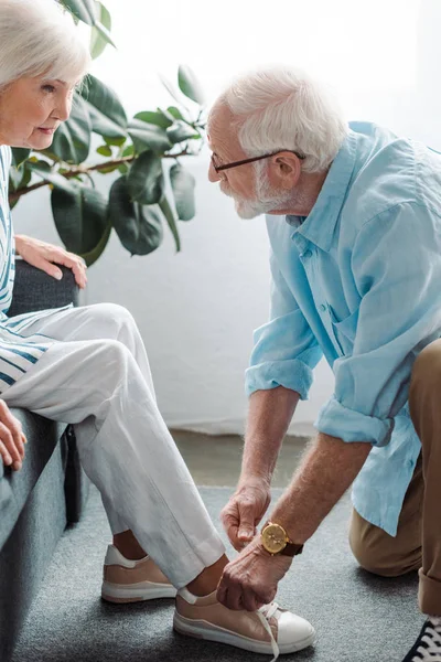 Side view of elderly man lacing shoe of wife on couch at home — Stock Photo