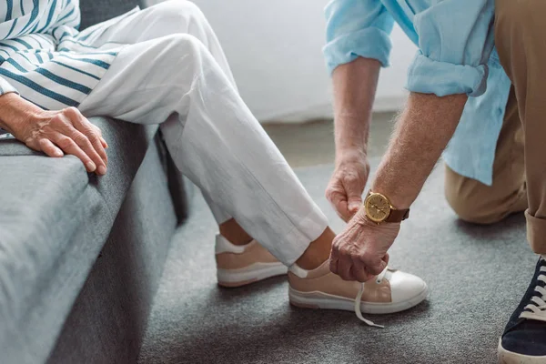 Ausgeschnittene Ansicht eines älteren Mannes, der Schuh einer Frau auf Couch schnürt — Stockfoto