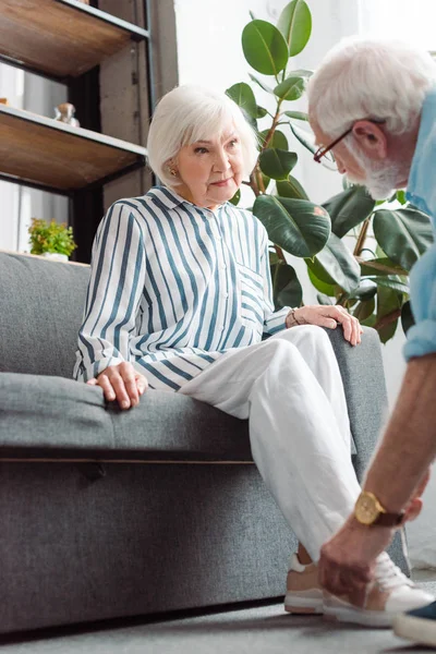 Selektiver Fokus der Seniorin auf Mann, der Schuh im Wohnzimmer schnürt — Stockfoto