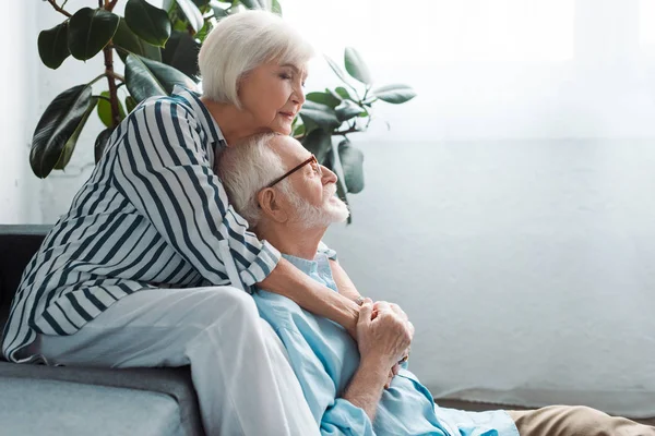 Vista lateral da mulher idosa abraçando marido no chão na sala de estar — Fotografia de Stock