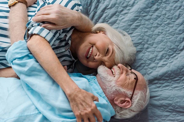 Vue du dessus du couple aîné souriant et étreignant sur le lit — Photo de stock