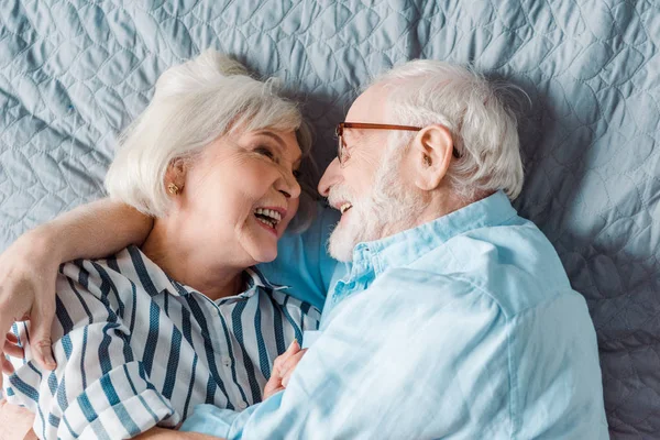 Вид сверху улыбающейся пожилой пары, улыбающейся, лежа на кровати — стоковое фото