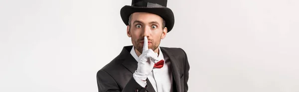 Panoramic shot of emotional magician in gloves showing silence symbol, isolated on grey — Stock Photo