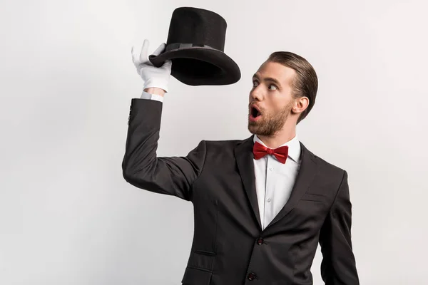 Shocked magician with open mouth looking at hat, isolated on grey — Stock Photo