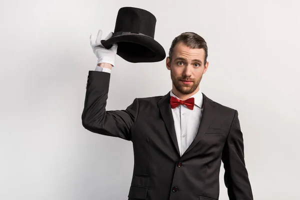 Емоційний фокусник в рукавичках тримає капелюх, ізольований на сірому — стокове фото