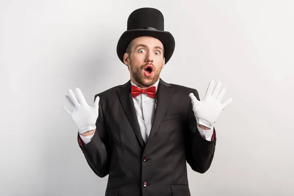 Mago en guantes y sombrero con gesto de encogimiento, aislado en gris - foto de stock