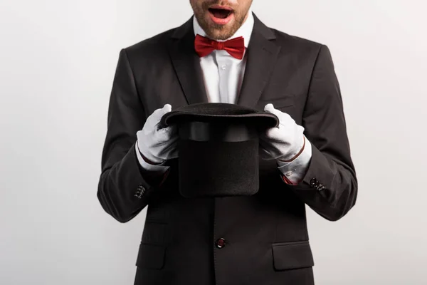 Cropped view of shocked magician holding hat, isolated on grey — Stock Photo