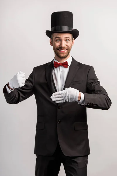 Mágico alegre mostrando truque com o dedo, isolado em cinza — Fotografia de Stock