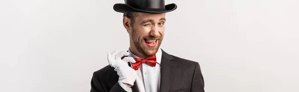 Panoramic shot of emotional magician winking and adjusting bow tie, isolated on grey — Stock Photo