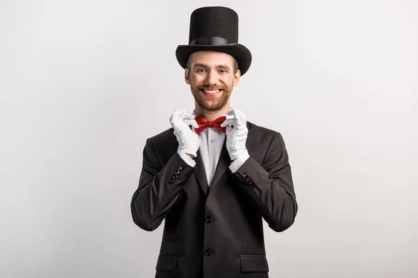 Красивий усміхнений чарівник, що регулює червону краватку з бантом, ізольований на сірому — стокове фото