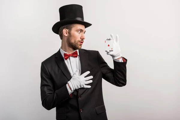 Mágico chocado olhando para jogar cartas, isolado em cinza — Fotografia de Stock