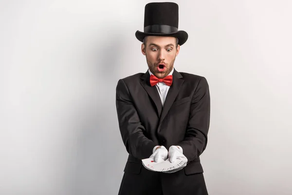 Excited magician with open mouth holding playing cards, on grey — Stock Photo