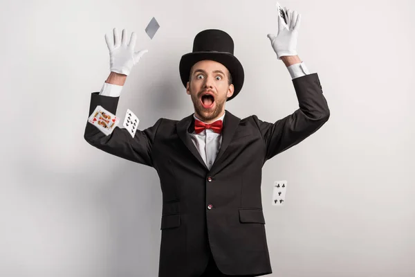 Surprised magician throwing playing cards, on grey — Stock Photo