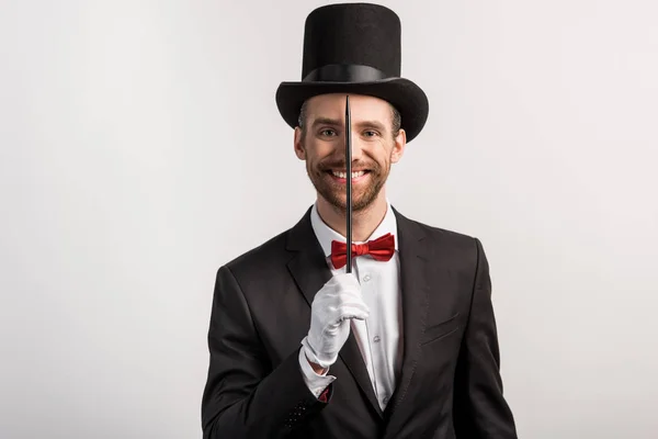 Mago alegre en traje y sombrero que sostiene la varita, aislado en gris - foto de stock