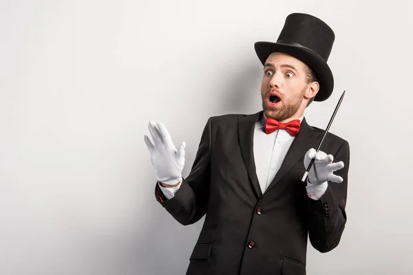 Shocked magician with open mouth holding wand, isolated on grey — Stock Photo