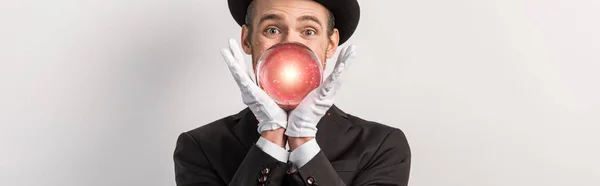 Plan panoramique d'un magicien émotionnel tenant une boule magique rouge, isolé sur du gris — Photo de stock