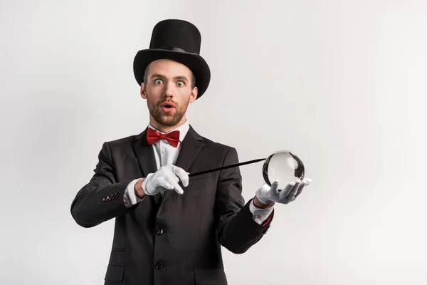 Surprised magician holding wand and magic ball, isolated on grey — Stock Photo