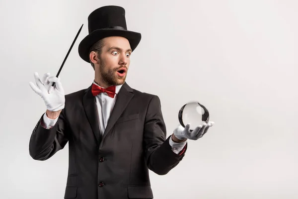 Magicien choqué tenant baguette magique et balle magique, isolé sur gris — Photo de stock
