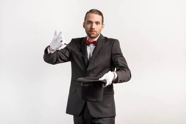 Magician in suit making trick hat and wand, isolated on grey — Stock Photo