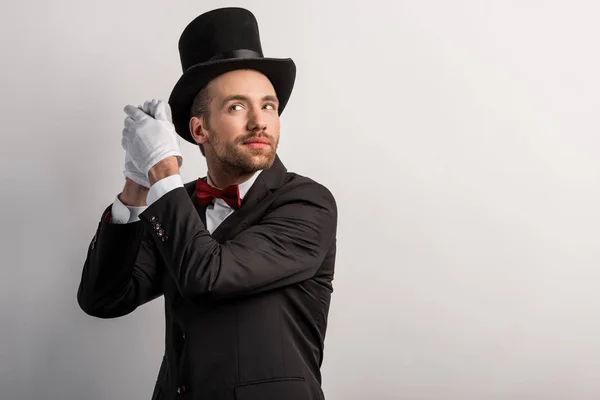 Magicien positif écoutant quelque chose dans les mains, isolé sur gris — Photo de stock