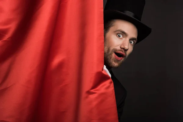 Beau magicien choqué en costume et chapeau dans le cirque avec des rideaux rouges — Photo de stock