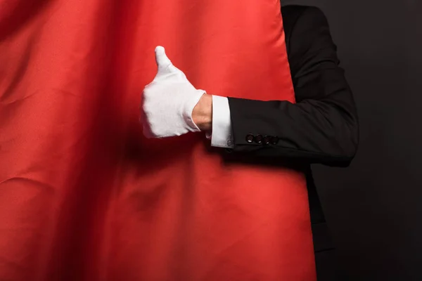 Cropped view of magician in glove showing thumb up in circus with red curtains — Stock Photo