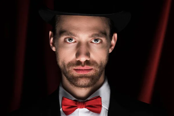 Handsome magician in suit and bow tie in circus with red curtains — Stock Photo