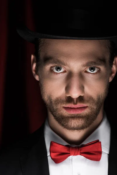 Beau magicien en costume, noeud papillon et chapeau dans le cirque avec des rideaux rouges — Photo de stock