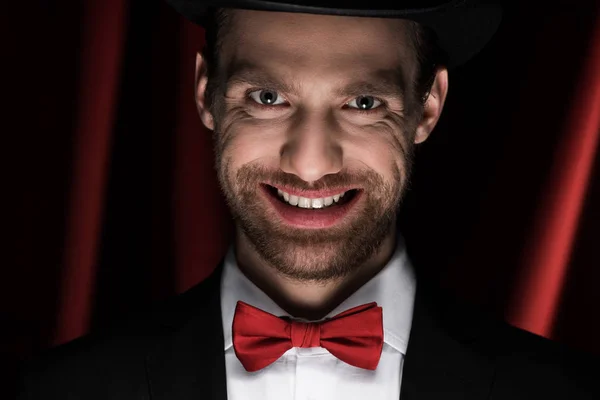 Assustador sorridente cavalheiro em terno e laço no circo com cortinas vermelhas — Fotografia de Stock