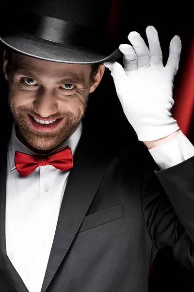 Scary smiling gentleman in suit and hat in circus with red curtains — Stock Photo