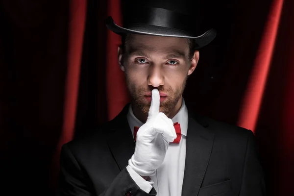 Zauberer zeigt Schweigesymbol im Zirkus mit roten Vorhängen — Stockfoto