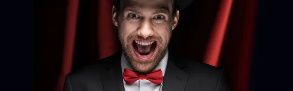 Panoramaaufnahme eines unheimlich aufgeregten Zauberers mit offenem Mund im Zirkus mit roten Vorhängen — Stockfoto