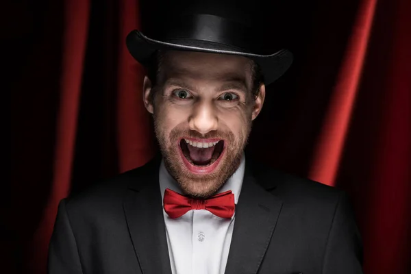 Scary excited magician with open mouth in circus with red curtains — Stock Photo