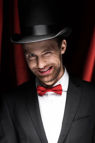 Smiling magician winking in circus with red curtains — Stock Photo