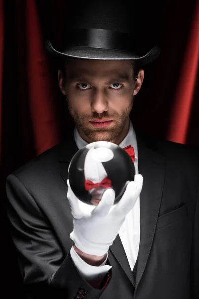 Professional magician holding magic ball in circus with red curtains — Stock Photo