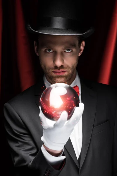 Professional magician holding red magic ball in circus with red curtains — Stock Photo