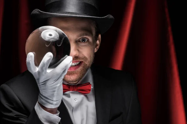 Smiling magician holding magic ball in circus with red curtains — Stock Photo
