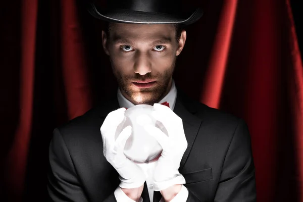 Professional magician holding magic ball in circus with red curtains — Stock Photo