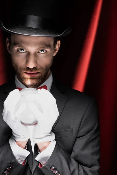 Professional magician holding magic ball in circus with red curtains — Stock Photo