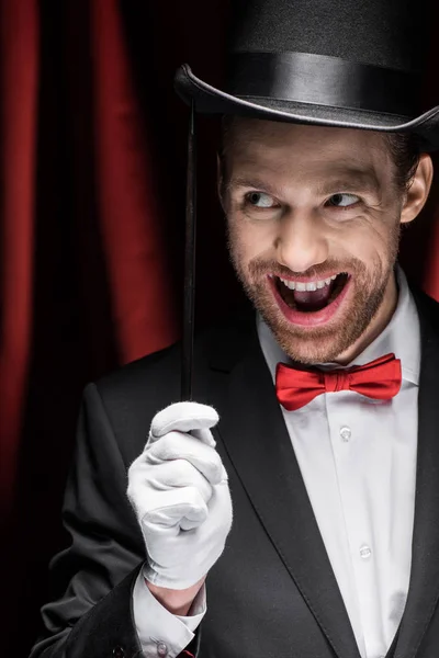 Magicien excité à bouche ouverte tenant baguette dans le cirque avec rideaux rouges — Photo de stock