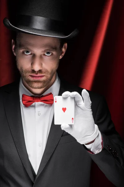 Professional magician holding playing cards in circus with red curtains — Stock Photo