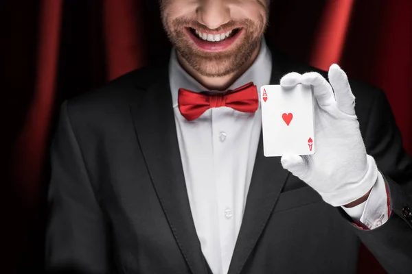 Cropped view of smiling magician holding playing cards in circus with red curtains — Stock Photo