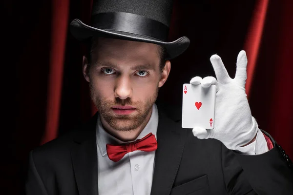 Magician holding playing cards in circus with red curtains — Stock Photo