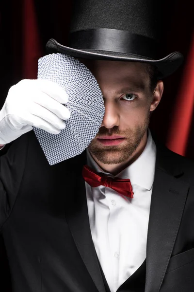 Magician holding playing cards in circus with red curtains — Stock Photo