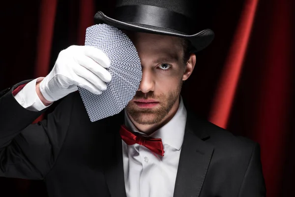 Mago profesional sosteniendo cartas en circo con cortinas rojas — Stock Photo