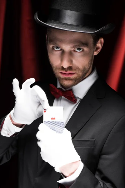 Серйозний фокусник тримає гральні карти в цирку з червоними шторами — стокове фото