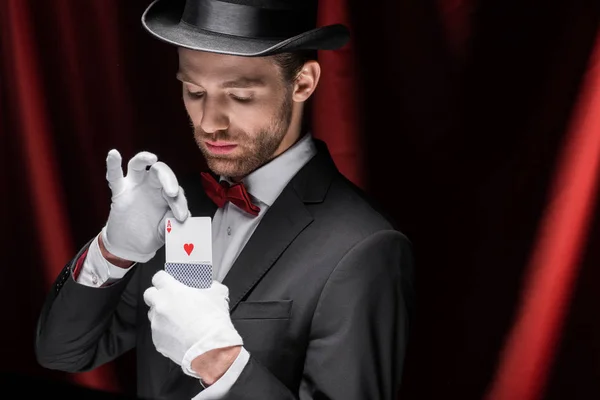 Magician holding playing cards in circus with red curtains — Stock Photo