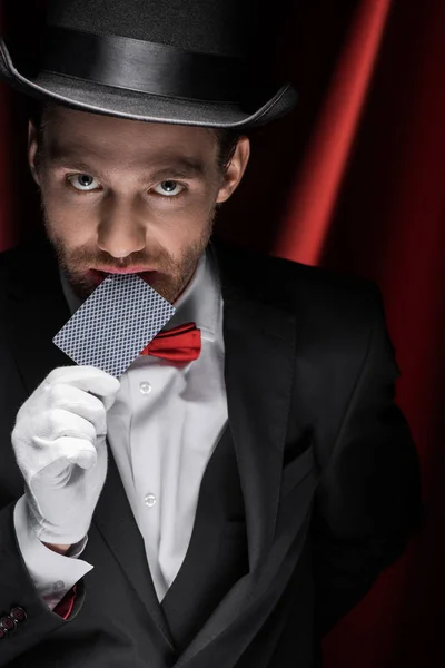 Profi-Zauberer zeigt Trick mit Spielkarte im Zirkus mit roten Vorhängen — Stockfoto